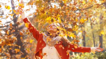 Frau streckt im Herbst in Falllaub ihre Arme nach oben
