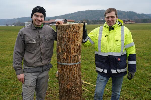 Zwei junge Männer stehen auf einer Wiese neben einem Holzpfahl