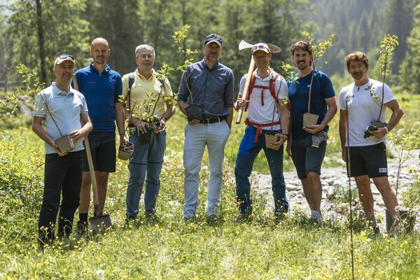 Gruppe von Männern mit Baumsetzlingen in der Hand auf einer Wiese 