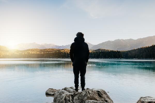 Man mit Rücken zur Kamera schaut auf einen See bei Sonnenaufgang