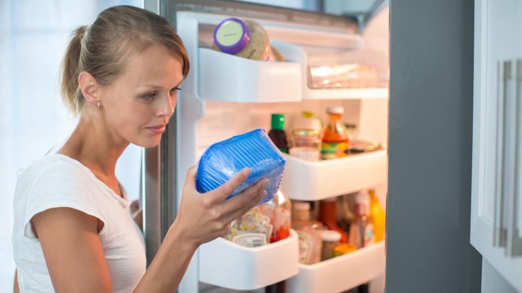Frau mit Lebensmittel vor geöffnetem Kühlschrank