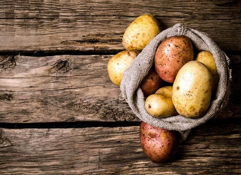 Kartoffeln mit unterschiedlicher Schalenfarbe in Korb auf einem Holztisch