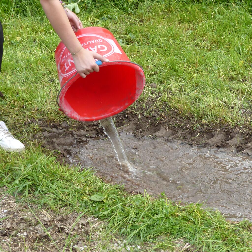 Lacke auffüllen © Johannes Maurer Ein Erdloch wird mit einem Kübel Wasser befüllt