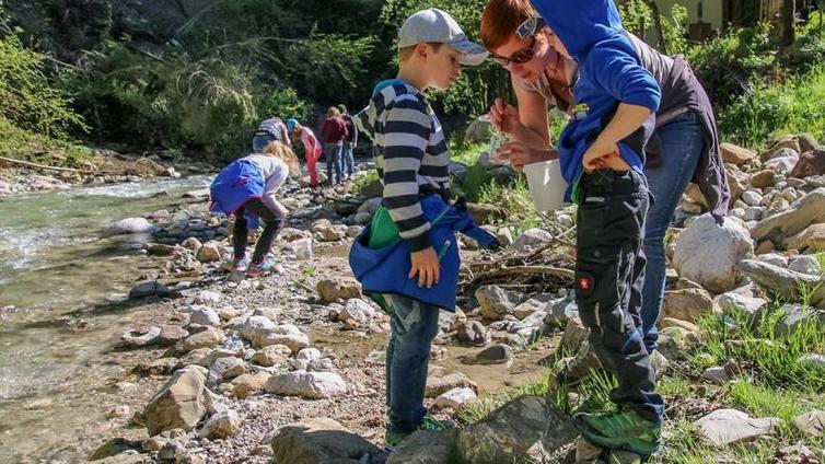 Auf der Suche nach den Wassermonstern stehen die Kinder am Bach und schauen durch Lupen auf die Unterseite von Bachsteinen