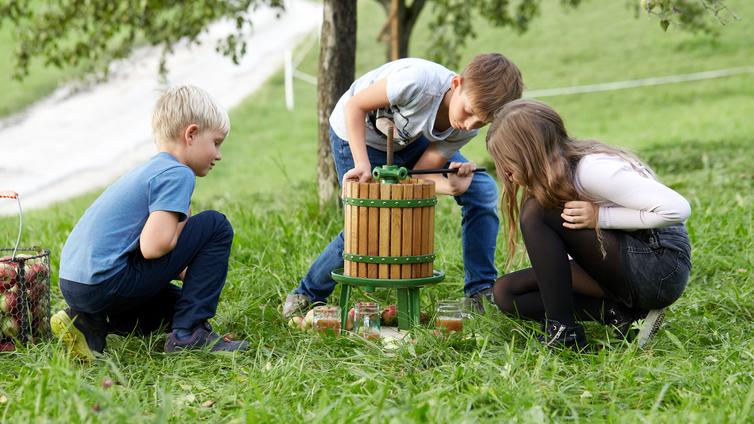 Schlaraffenland Streuobstwiese © NUPAT_Daniela Stockinger drei Kinder pressen Obstsaft an einer kleinen mobilen Obstpresse