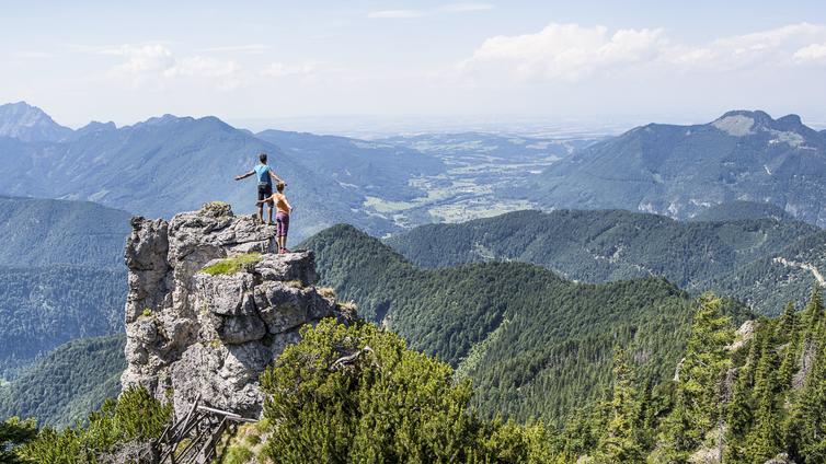 Zwei Personen stehen mit ausgebreiteten Armen auf einem Felsen über dem Wald-Paradies.