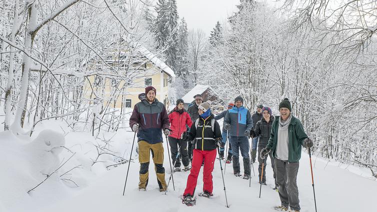 Eine Gruppe von Schneeschuh-Wanderern im tief verschneiten Wald vor der Böhmerwaldschule.