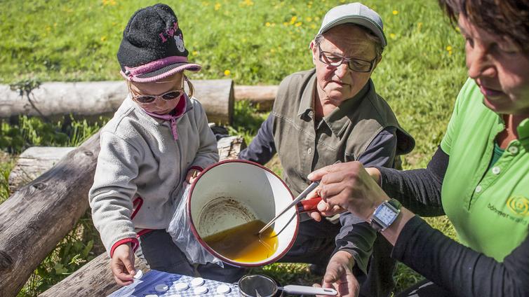 Zwei Erwachsene und ein Kind bereiten eine Pechsalbe zu und füllen sie in ein Gefäß ab.