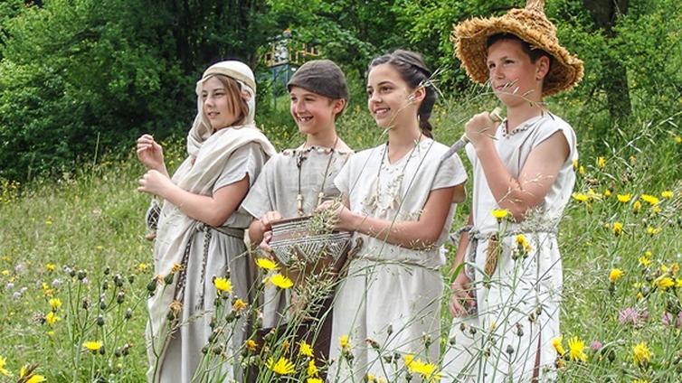 Pfahlbau am Attersee - Das Leben im Pfahlbaudorf © NATURSCHAUSPIEL, Gerald Egger 4 Kinder stehen in steinzeitlicher Kleidung in einer Wiese am Ufer des Attersses