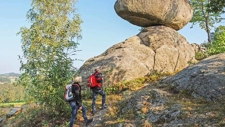 Zwei Wanderer betrachten einen großen Granitblock am Weg.