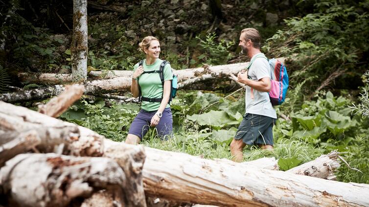 Eine Frau und ein Mann gehen durch einen Wald mit umgestürzten Baumstämmen