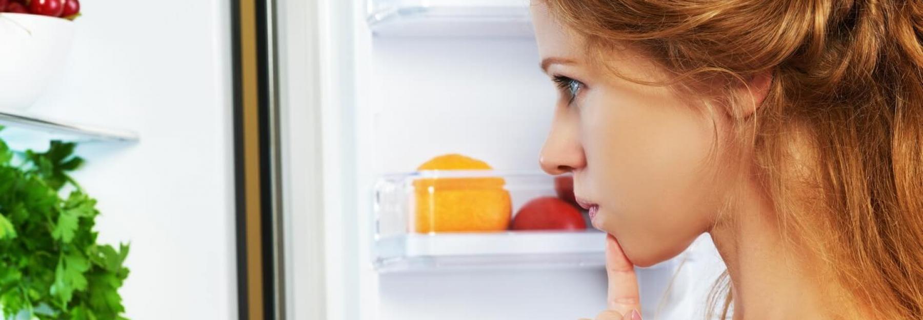 Frau steht vor offenem Kühlschrank (c)