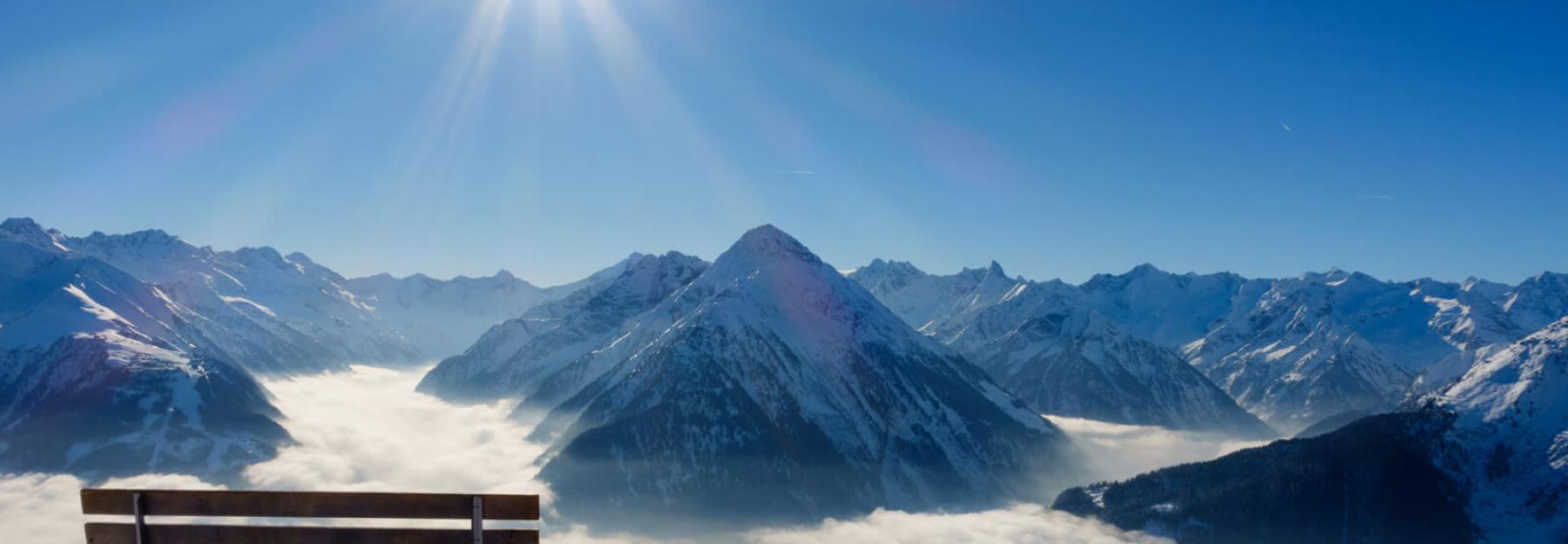 Bank in den schneebedeckten Bergen mit Ausblick auf Sonne und Gipfel