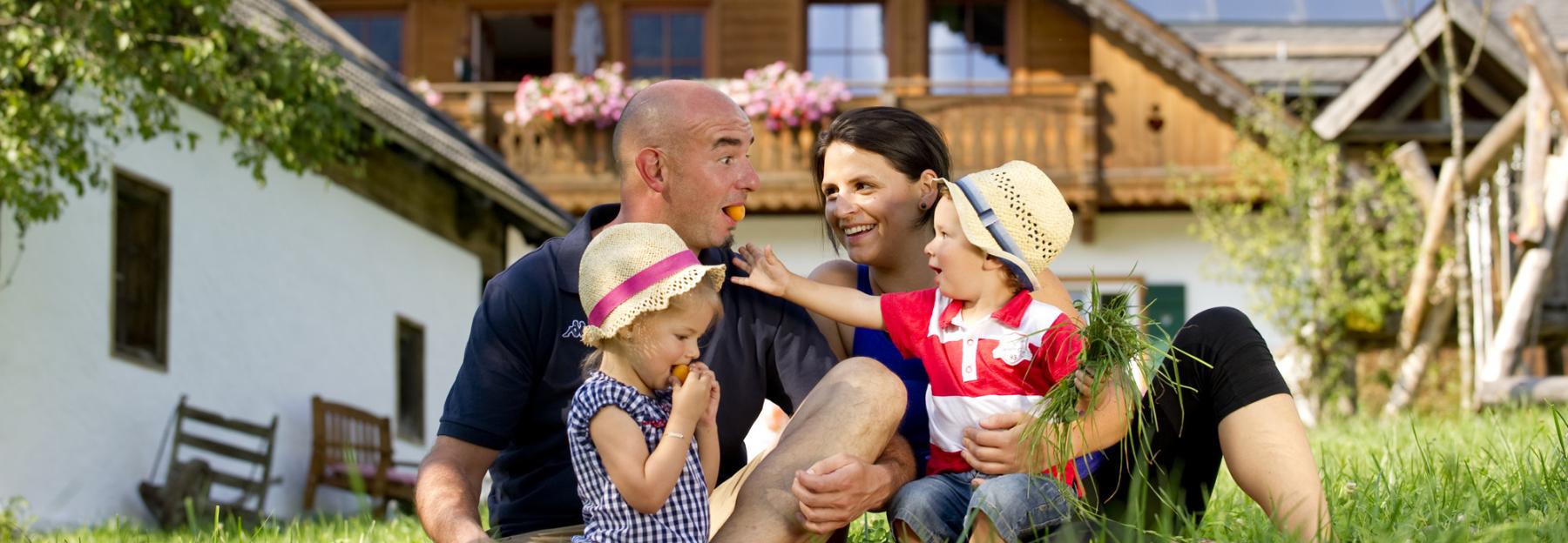 Familie sitzt in der Wiese vor einem Bauernhof