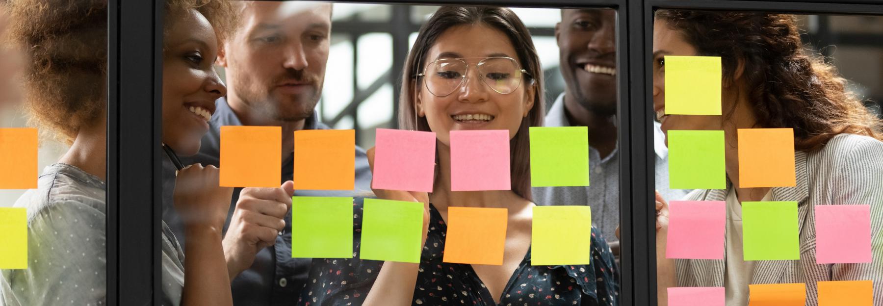Junge Leute arbeiten mit Post-its auf Fensterscheibe