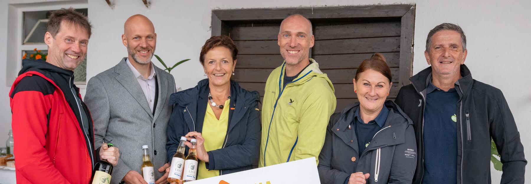 Sechs Menschen stehen nebeneinander mit Apfelsatzflaschen 