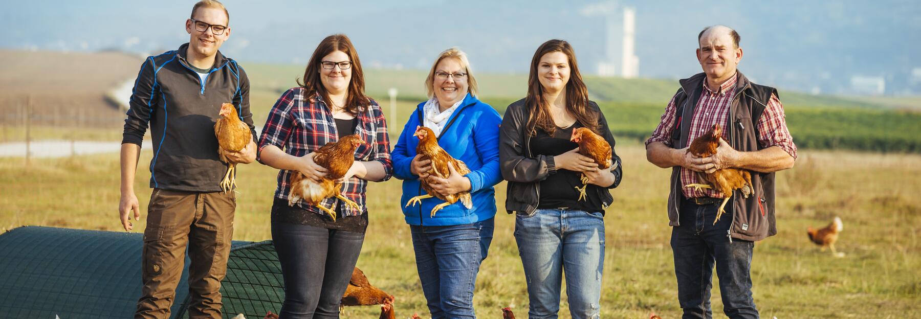 Familienfoto von LandwirtInnen, die nebeneinander mit Hühnern auf einem Feld stehen