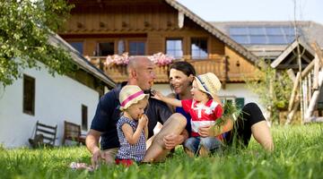 Familie sitzt in der Wiese vor einem Bauernhof