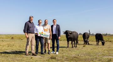Vier Menschen stehen mit drei Wasserbüffeln im Hintergrund auf einer grünen Wiese