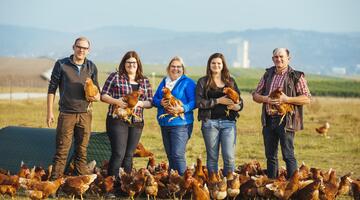 Familienfoto von LandwirtInnen, die nebeneinander mit Hühnern auf einem Feld stehen
