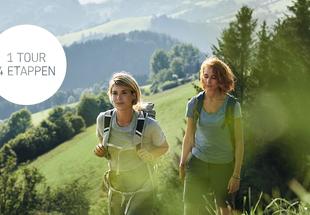 Zwei junge Frauen wandern durch die grüne Hügellandschaft des Ennstales.