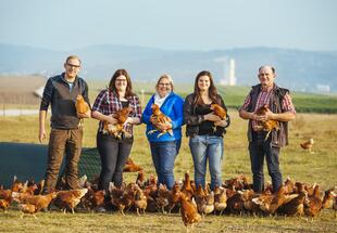 Familienfoto von LandwirtInnen, die nebeneinander mit Hühnern auf einem Feld stehen